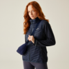 Vrouw met rood haar draagt een navy doorgestikte bodywarmer, donker shirt, donkere legging en een klein schoudertasje voor een lichte achtergrond