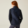 Persoon met rood haar van achteren gezien, draagt een marineblauwe, gewatteerde bodywarmer, donker shirt met lange mouwen en een diagonale tasriem, lichte achtergrond