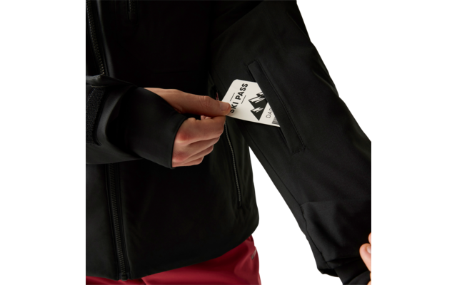 Hände einer Person in schwarzer Jacke, die eine weiße Karte mit Aufdruck "SKI PASS" in einer Reißverschlusstasche am Ärmel hält