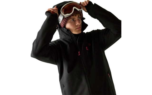 Person in schwarzer Skijacke und Strickmütze setzt eine Skibrille auf, heller Hintergrund