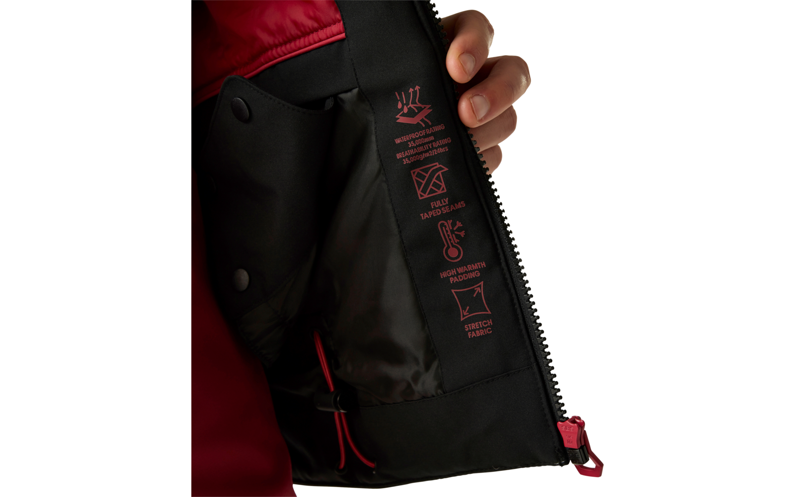 Hand hält Innenklappe einer Jacke offen, schwarze Innenfütterung mit roten Symbolen und offenem Reißverschluss