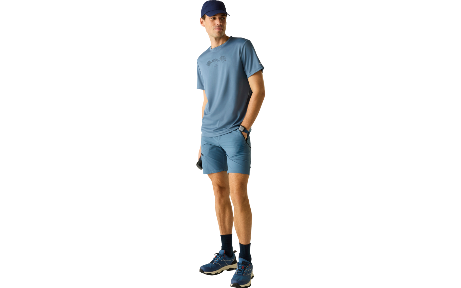 Mann in blauem Sportoutfit mit Kappe, T‑Shirt, Shorts, dunklen Socken und Sportschuhen, steht und blickt nach rechts, eine Hand in der Hosentasche