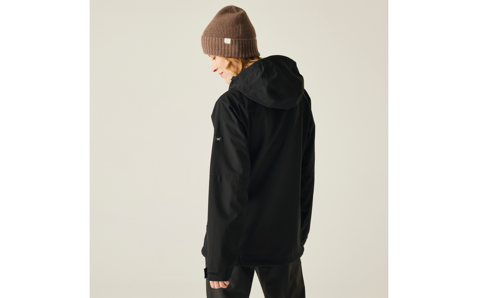 Person von hinten, trägt schwarze Kapuzenjacke und braune Mütze