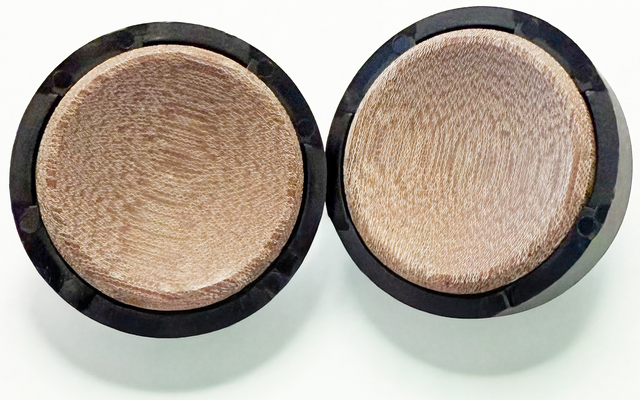 Due coppette rotonde con polvere beige dalla superficie finemente strutturata e bordi neri su sfondo bianco