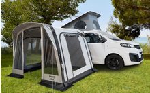 White camper with open rooftop tent and attached gray awning, standing on green grass under trees