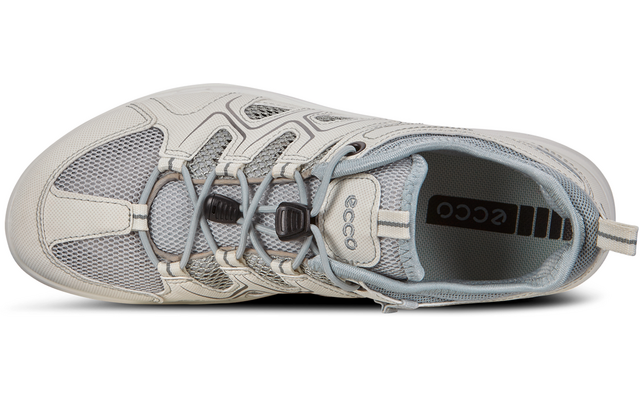 Vista superior de una zapatilla gris claro/crema con paneles de malla, cordones y logo "ecco" visible en la lengüeta y la plantilla