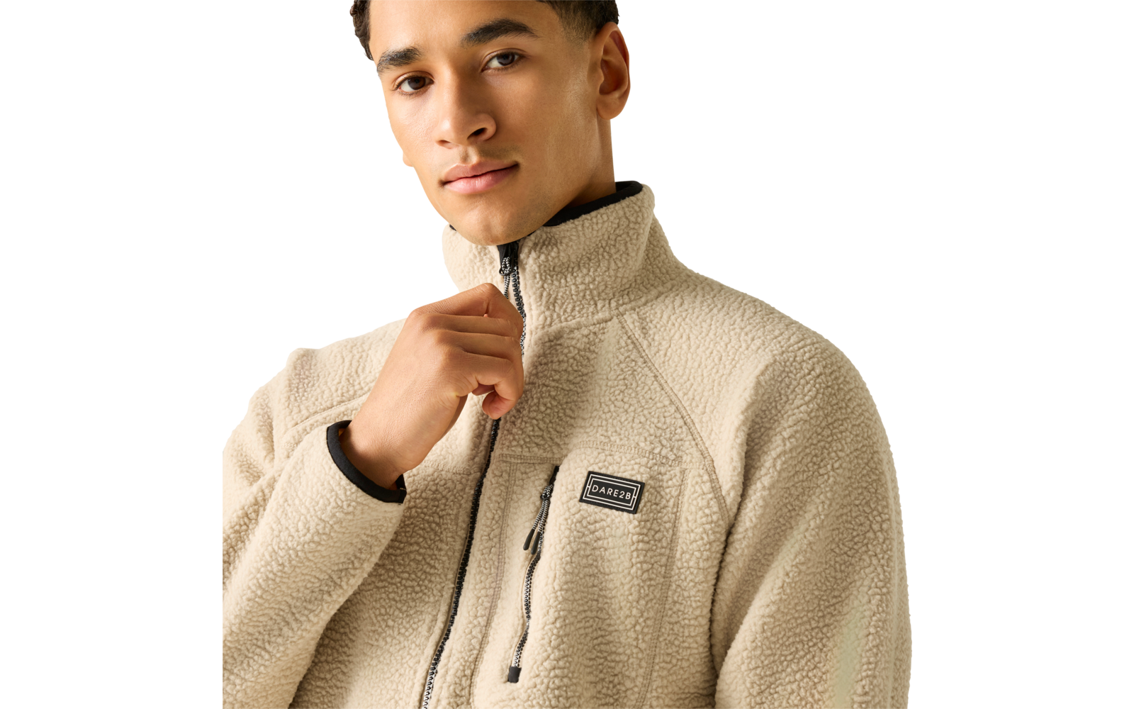 Person von Brust bis Kopf, trägt beige Teddy‑Fleecejacke mit hohem Kragen, rechte Hand am Reißverschluss, sichtbares Logo auf der Brust, heller einfarbiger Hintergrund