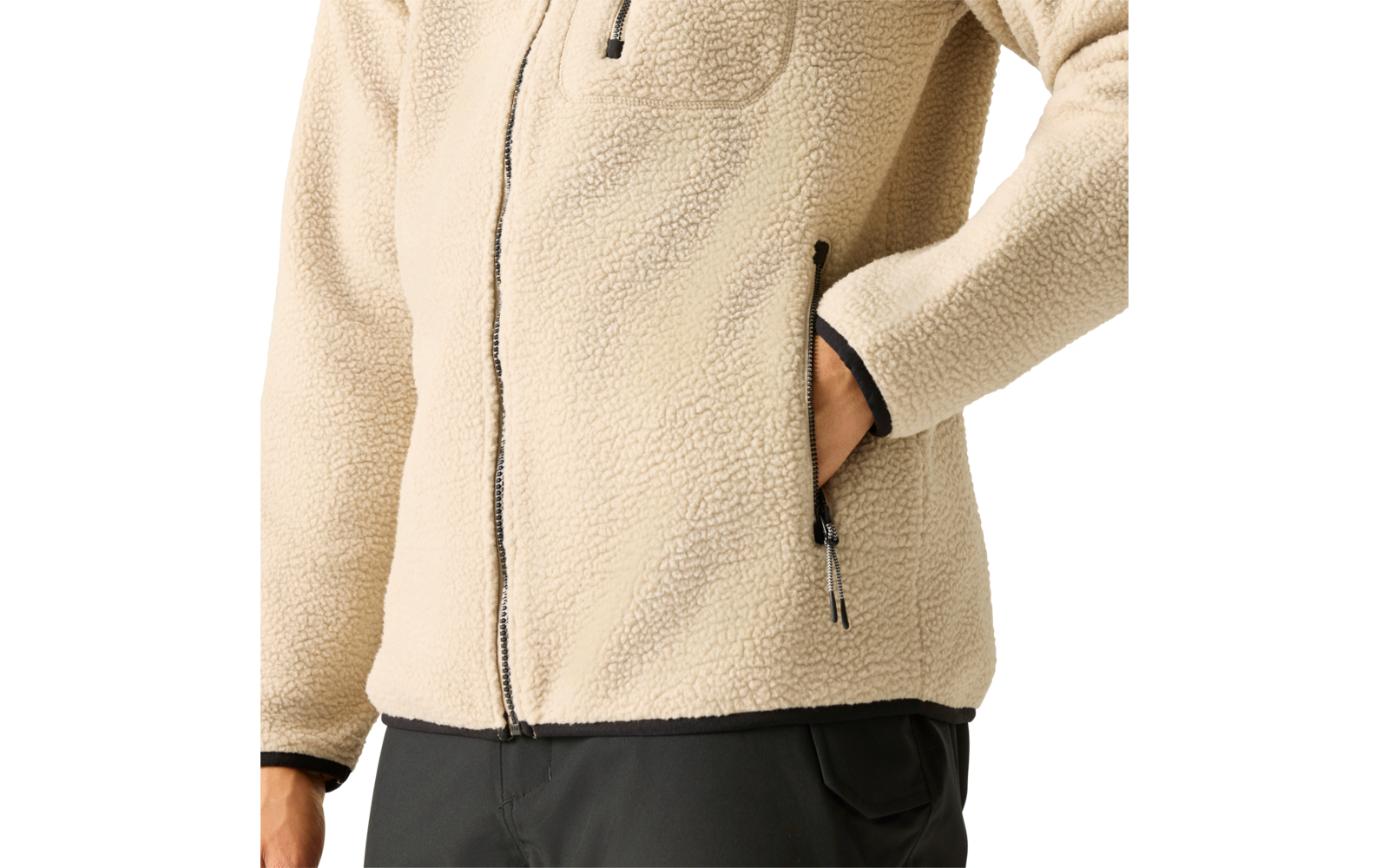 Teilansicht eines Oberkörpers in einer beige Fleecejacke mit Reißverschluss, Hand in einer Reißverschlusstasche; schwarze Hose sichtbar