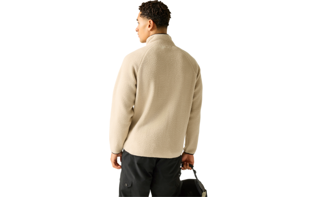 Person von hinten, kurz lockiges dunkles Haar, trägt beige Fleecejacke mit Stehkragen und schwarze Hose, hält schwarze Tasche in der rechten Hand, Kopf leicht nach links gedreht