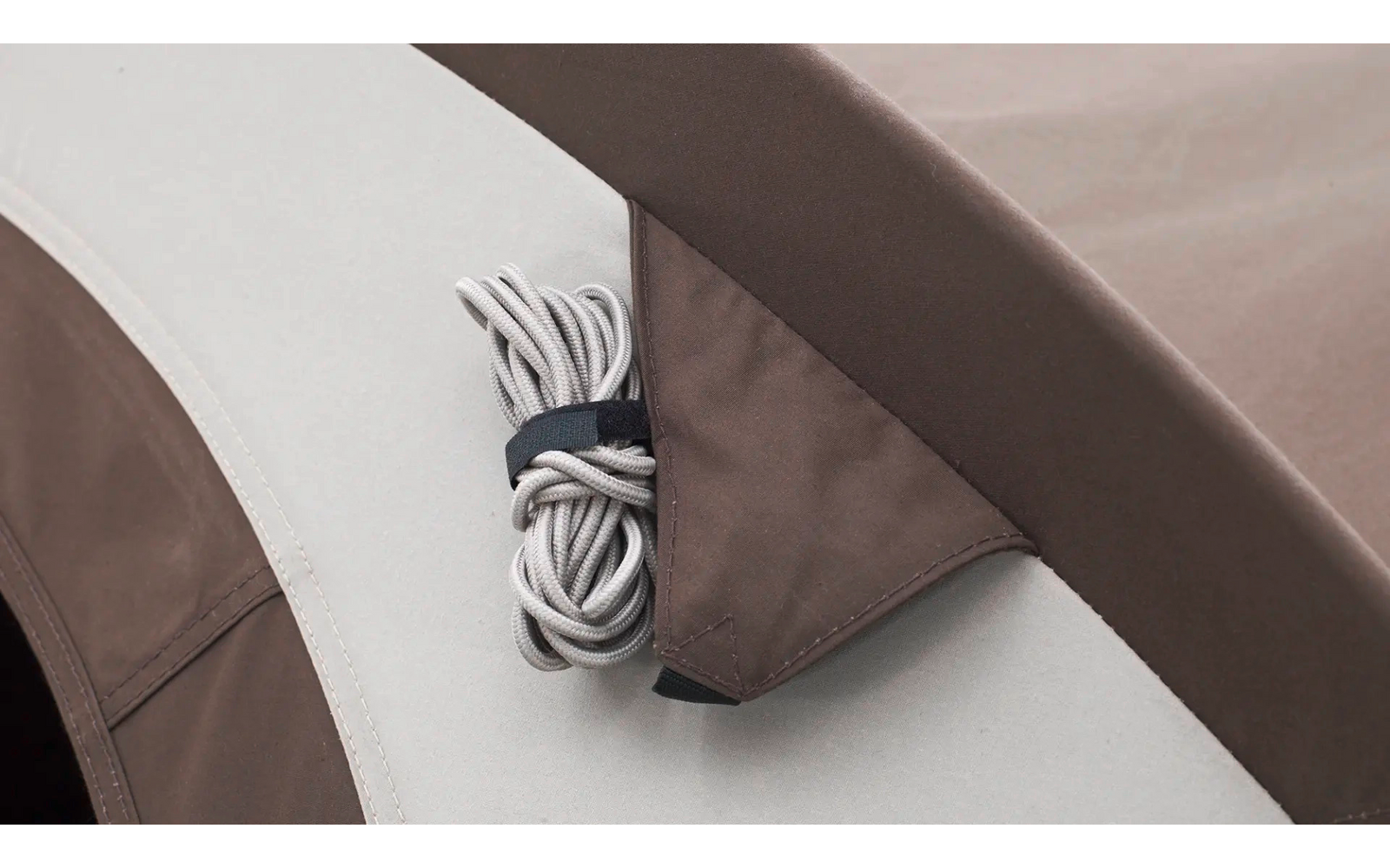 Nahaufnahme eines zusammengerollten weißen Kabels, mit schwarzem Band gebündelt, in einer braunen Stofftasche auf einer beige-braunen Oberfläche