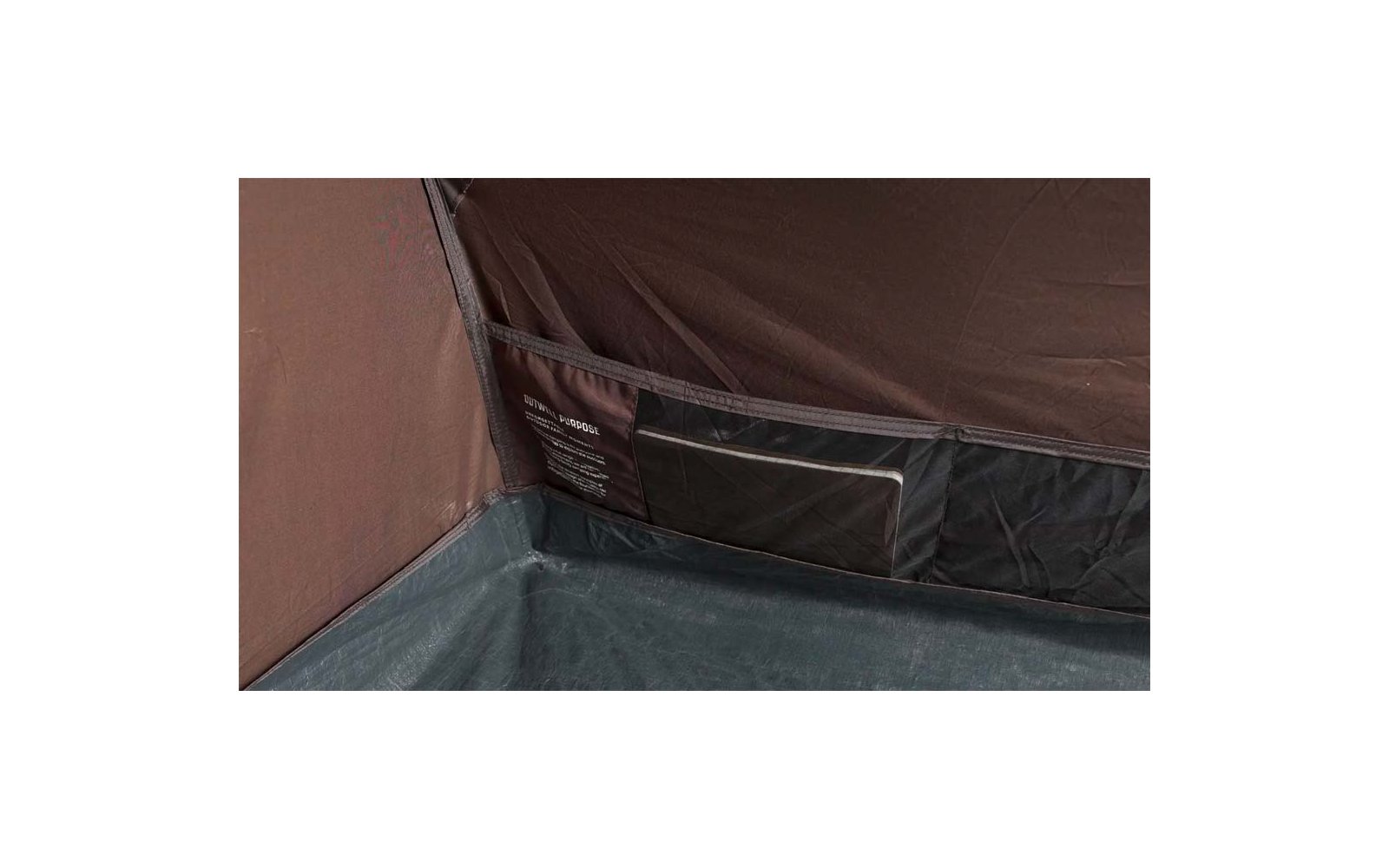 Ecke eines Innenraums aus dunkelbraunem Stoff mit grauem Boden, eingenähter Tasche mit transparentem Fenster und Etikett