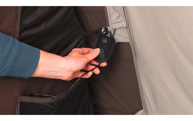 Hand hält kleines schwarzes Gerät mit Knopf und Kabel neben grauem Stoffrand