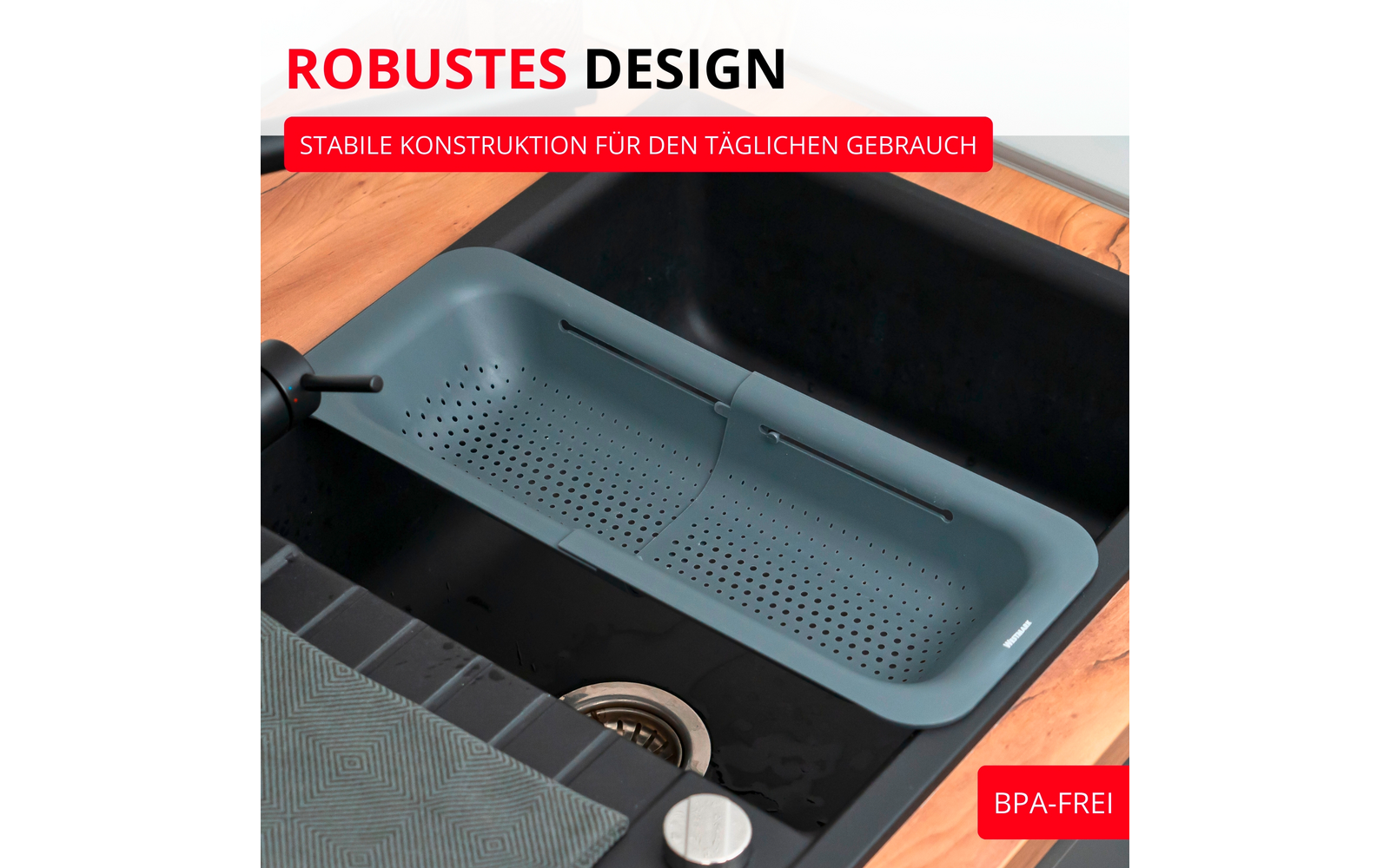 Passoire en silicone gris‑vert au‑dessus d'un évier de cuisine noir dans un plan de travail en bois, bonde en acier inoxydable visible, robinet à gauche, torchon plié et bandes de texte rouges 'ROBUSTES DESIGN' et 'BPA-FREI'