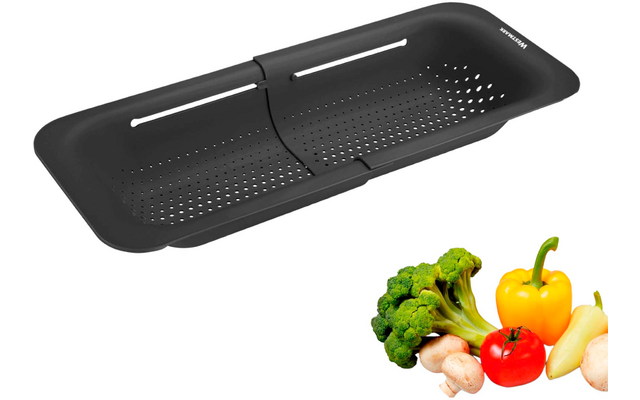 Passoire rectangulaire noire avec perforations, pli central et longues fentes latérales ; à côté, brocoli, un poivron jaune, une tomate rouge et deux champignons sur fond blanc