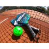 Zwei Padel-Schläger mit blau-weißem Muster liegen auf einem Tennisplatz, davor liegt ein grüner Ball