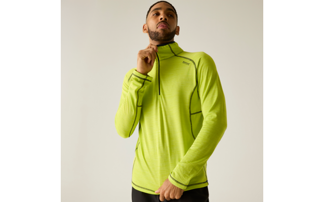 Personne portant un haut de sport vert néon à manches longues avec une courte fermeture éclair, tire la fermeture, debout devant un fond uni clair