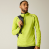 Personne devant un fond uni clair, portant un haut à manches longues vert néon avec une courte fermeture éclair au col, un sac à dos noir sur une épaule et un pantalon noir, regardant légèrement vers la droite