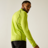 Personne portant un haut de sport vert fluo à manches longues et un pantalon noir, de profil, regardant par-dessus l'épaule sur un fond uni clair