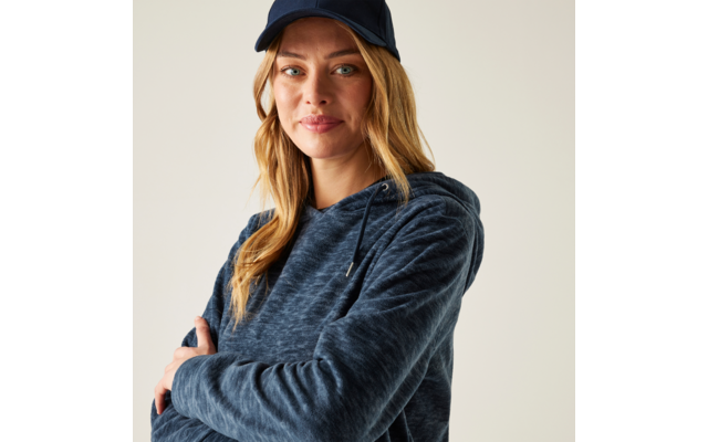 Frau mit blonden Haaren, dunkelblauer Baseballkappe und blauem Kapuzenpullover, mit verschränkten Armen, Blick zur Kamera