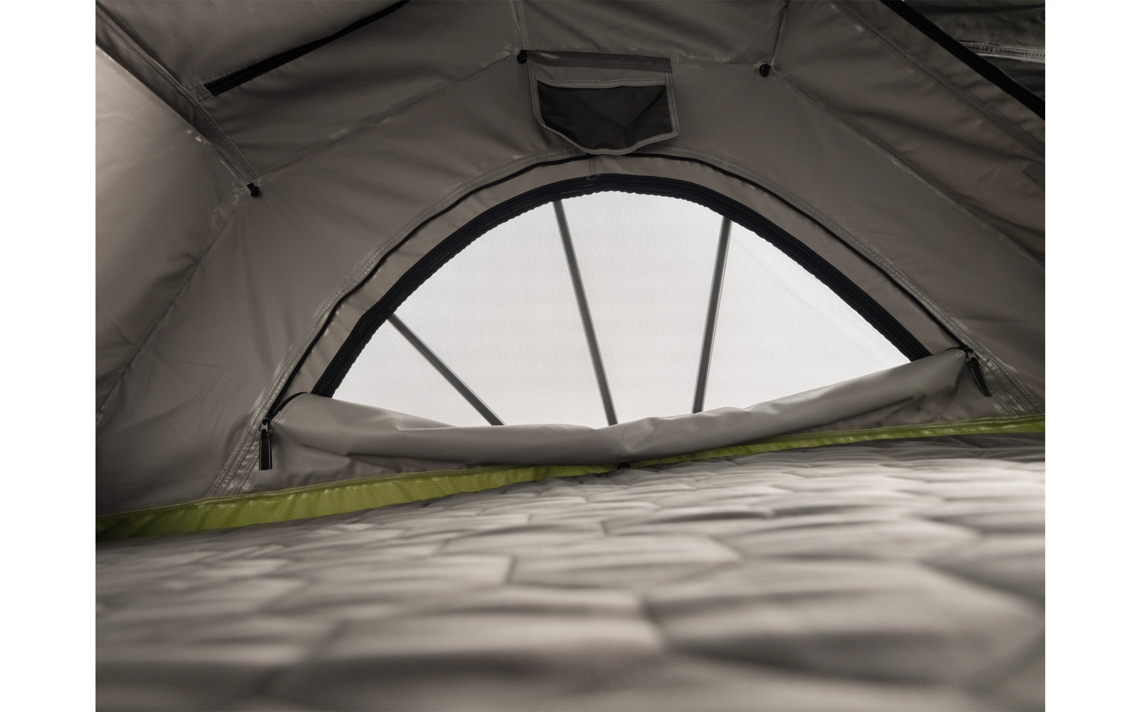 Innenansicht eines Zeltes mit halbkreisförmigem Netzfenster, kleiner Innentasche oben und einer grauen Isomatte mit grünem Rand im Vordergrund