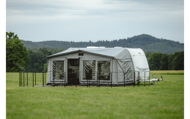 Zelt auf einer grünen Wiese mit Bäumen und Hügeln im Hintergrund