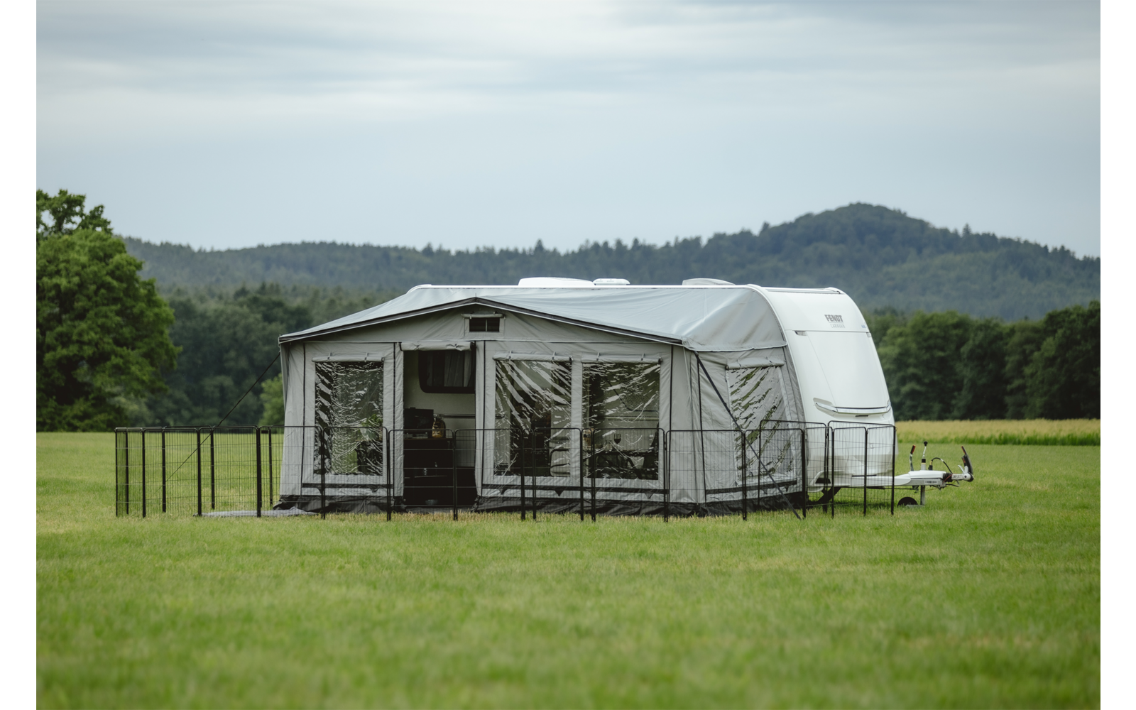 Zelt auf einer grünen Wiese mit Bäumen und Hügeln im Hintergrund