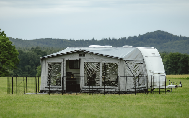 Zelt auf einer grünen Wiese mit Bäumen und Hügeln im Hintergrund