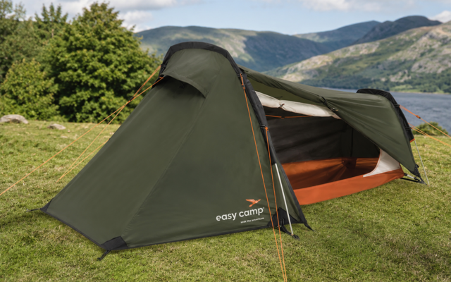 Groene tunneltent met open ingang en oranje binnenzijde, 'easy camp'-logo, op gras bij een meer en bergen