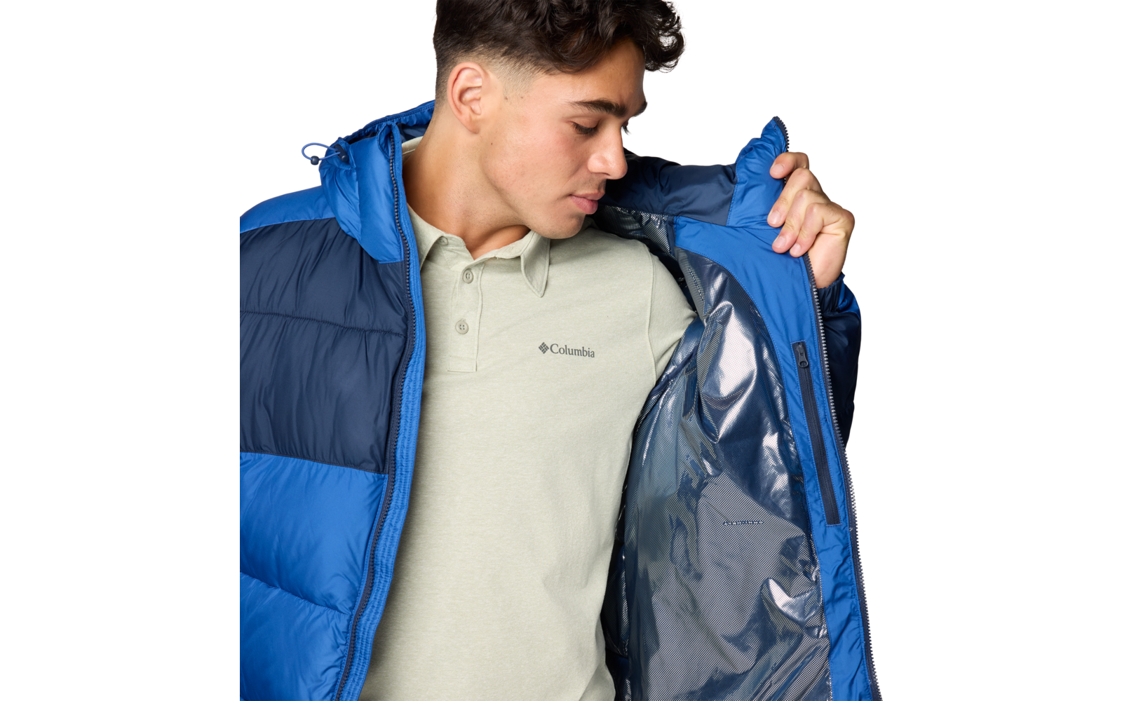Person trägt blaue Steppjacke, hält sie geöffnet und zeigt silbernes Innenfutter; darunter helles Poloshirt mit Columbia-Logo