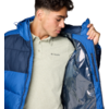 Person trägt blaue Steppjacke, hält sie geöffnet und zeigt silbernes Innenfutter; darunter helles Poloshirt mit Columbia-Logo