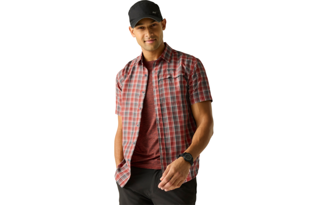 Person steht vor hellem einfarbigem Hintergrund, trägt schwarze Baseballkappe, rotes T-Shirt unter rotem kariertem Kurzarmhemd, schwarze Hose und Armbanduhr