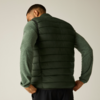 Personne vue de dos portant une doudoune sans manches matelassée vert foncé sur un haut manches longues vert clair, mains sur les hanches, pantalon noir, fond uni clair