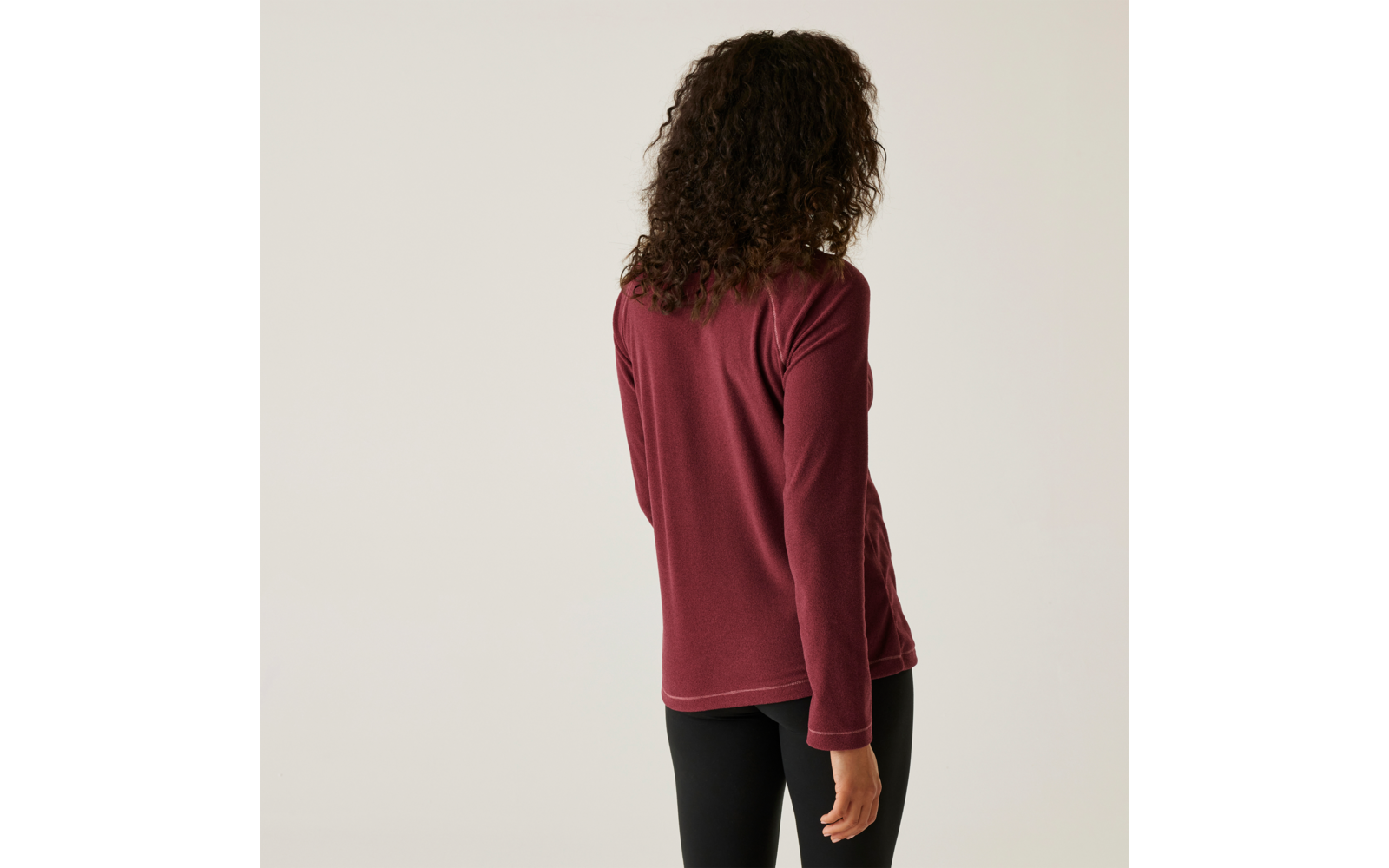 Frau mit lockigem Haar, die von hinten zu sehen ist, trägt ein rotes Langarmshirt und schwarze Hose