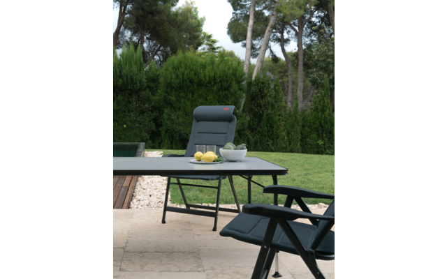 Ein grüner Garten mit einem schwarzen Tisch und zwei schwarzen Stühlen, auf dem Tisch steht eine Schale mit Zitronen