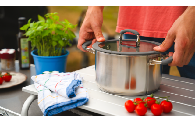 Person steht vor Herd und hält einen Topf mit Deckel