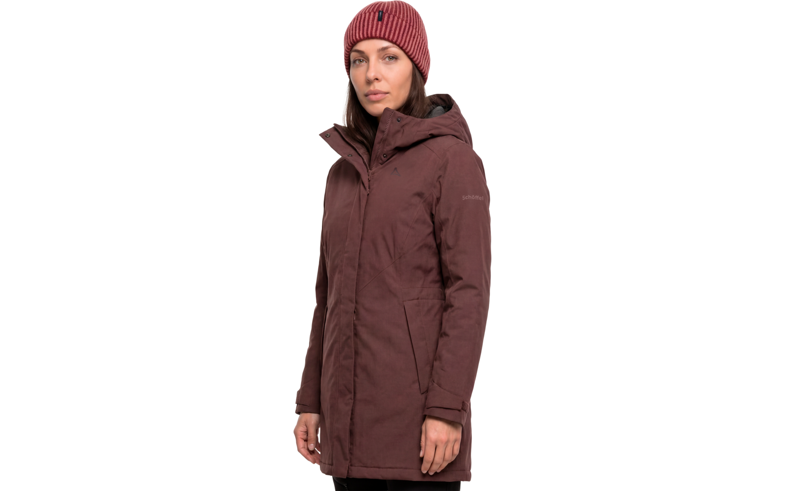 Persoon voor witte achtergrond draagt een bordeauxrode parka met capuchon en een rode gebreide muts; gezicht en handen zichtbaar