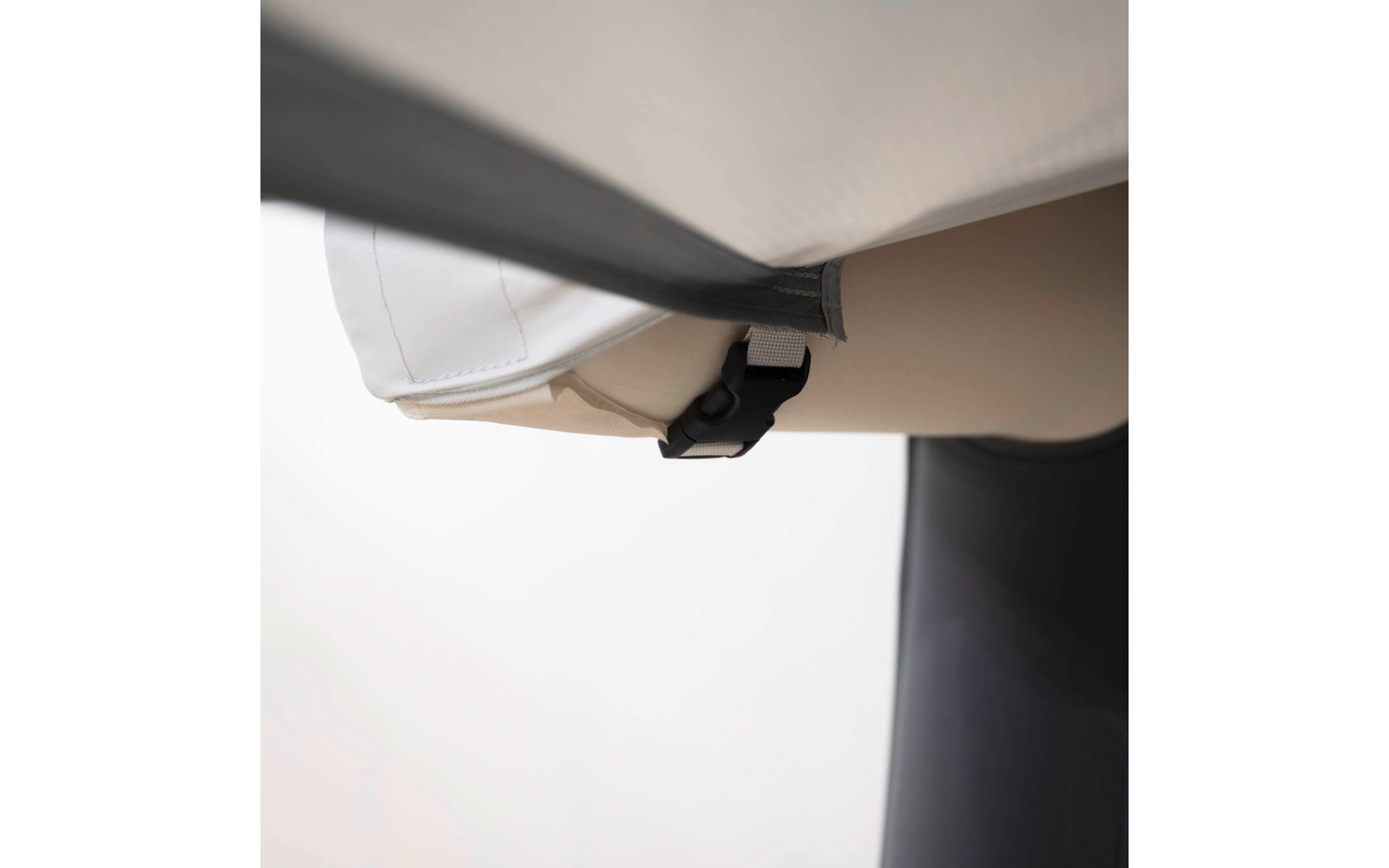 Nahaufnahme einer beige-weißen Polsterhülle mit grauem Gurt und schwarzem Kunststoffverschluss, im Hintergrund ein rundes schwarzes Bauteil