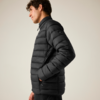 Person im Profil, trägt eine schwarze gesteppte Jacke mit hohem Kragen, Hände in den Taschen, heller Hintergrund