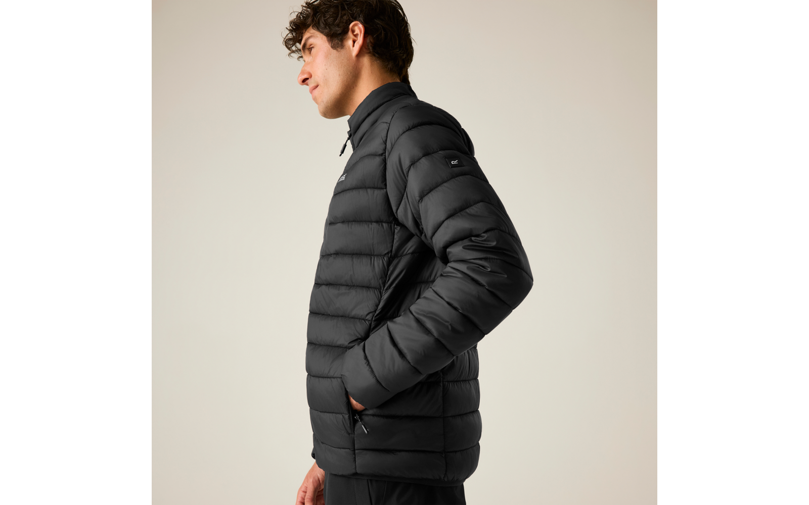 Person im Profil, trägt eine schwarze gesteppte Jacke mit hohem Kragen, Hände in den Taschen, heller Hintergrund