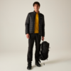 Stehende Person, schwarze gesteppte Jacke, gelbes Sweatshirt, schwarze Hose und Schuhe, hält schwarzen Rucksack in einer Hand, heller neutraler Hintergrund