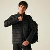 Ein Mann mit dunklen Haaren trägt eine schwarze gesteppte Jacke und einen Rucksack, er hält den Reißverschluss und blickt nach rechts vor hellem Hintergrund