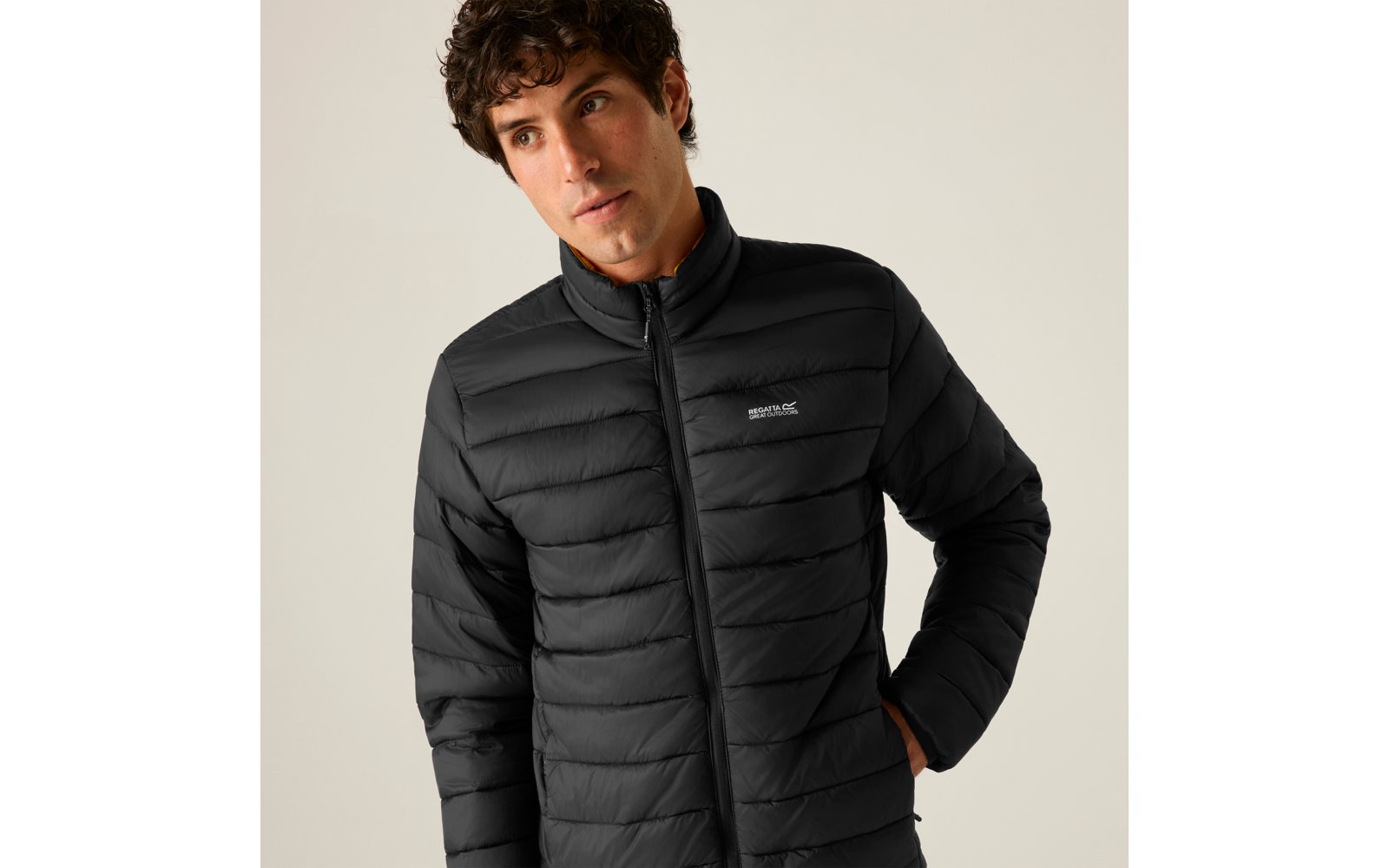 Ein Mann trägt eine schwarze gesteppte Jacke mit Stehkragen, rechte Hand in der Tasche, Blick nach links