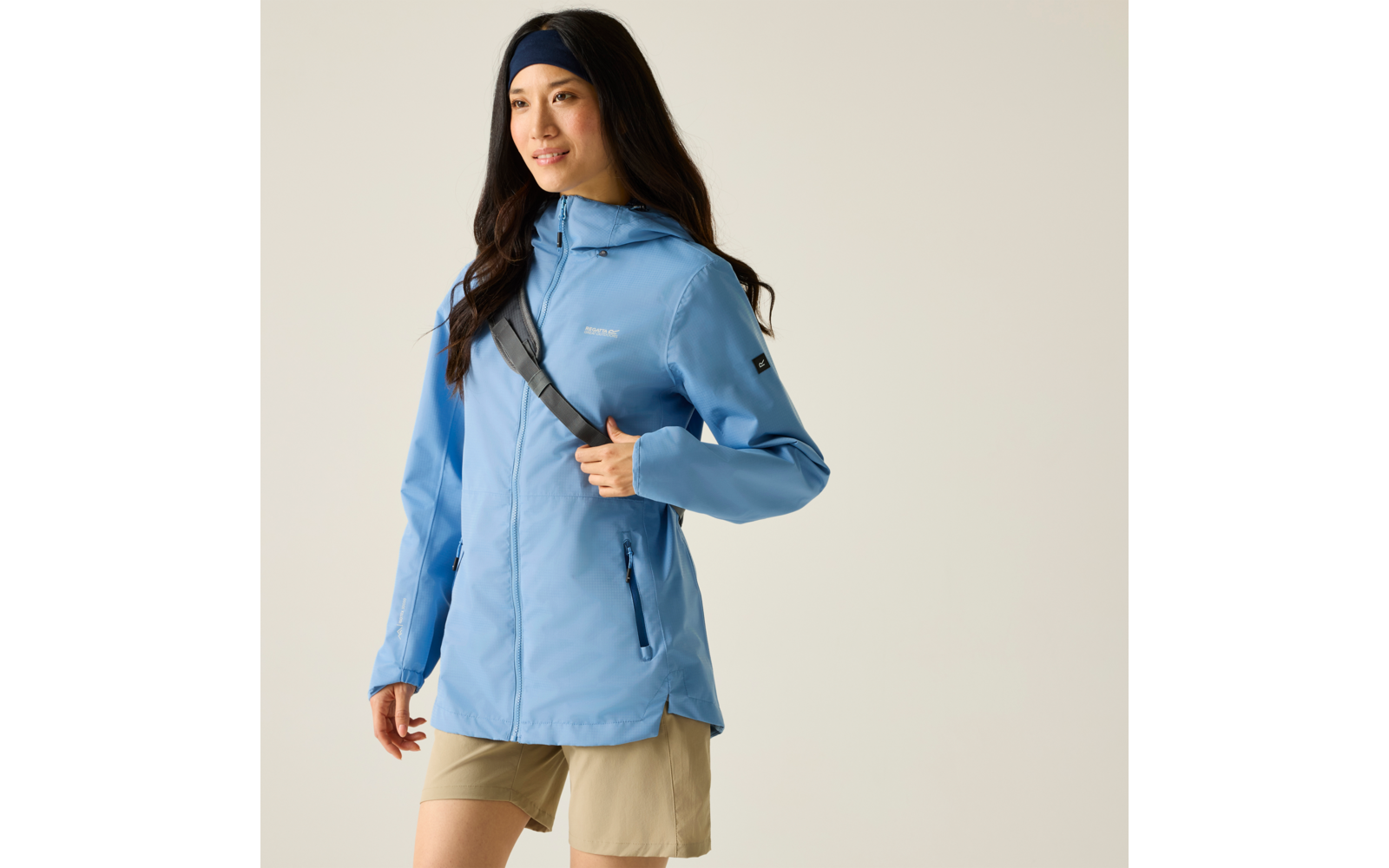 Person in hellblauer Kapuzenjacke und beigen Shorts, schwarzes Stirnband, Schulterriemen, steht und hält den Riemen