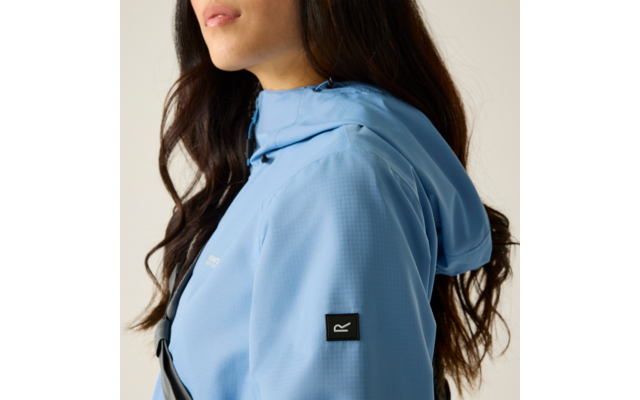 Seitliche Ansicht einer Person von Kinn bis Schulter mit langen dunklen Haaren, trägt eine hellblaue Kapuzenjacke mit schwarzem quadratischem Logo auf dem Ärmel und einem schwarzen Schultergurt; heller Hintergrund