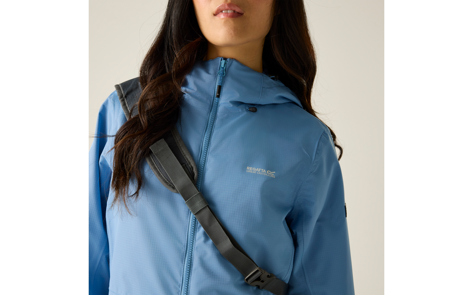 Oberkörper einer Person in hellblauer, geschlossener Kapuzenjacke mit schräg über der Brust verlaufendem Taschenriemen