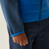 Close-up van een persoon met een blauwe jas en donkere broek, rechterhand zichtbaar