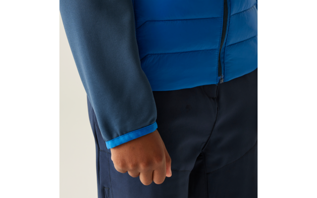 Close-up van een persoon met een blauwe jas en donkere broek, rechterhand zichtbaar