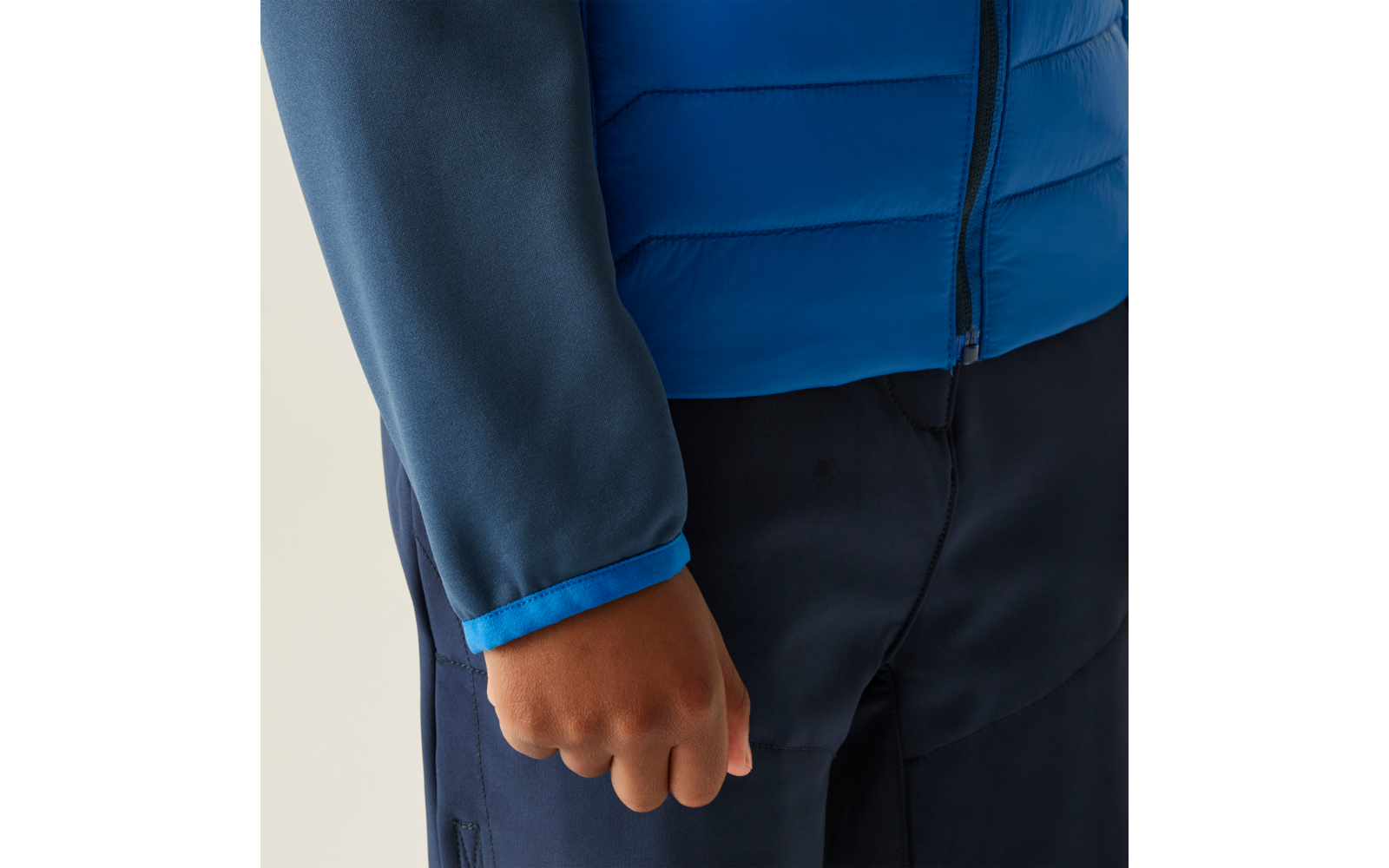 Close-up van een persoon met een blauwe jas en donkere broek, rechterhand zichtbaar