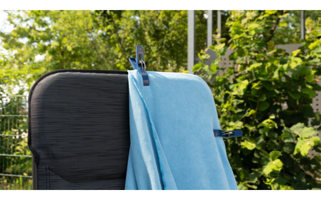 Blauer Mund-Nasen-Schutz liegt auf schwarzem Stuhl im Außenbereich mit grünen Pflanzen im Hintergrund