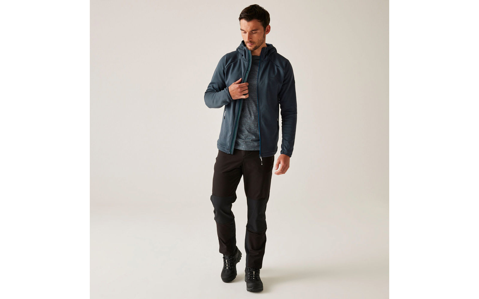 Ein Mann trägt eine blaue Jacke, ein blaues Hemd und schwarze Hose, er geht nach rechts